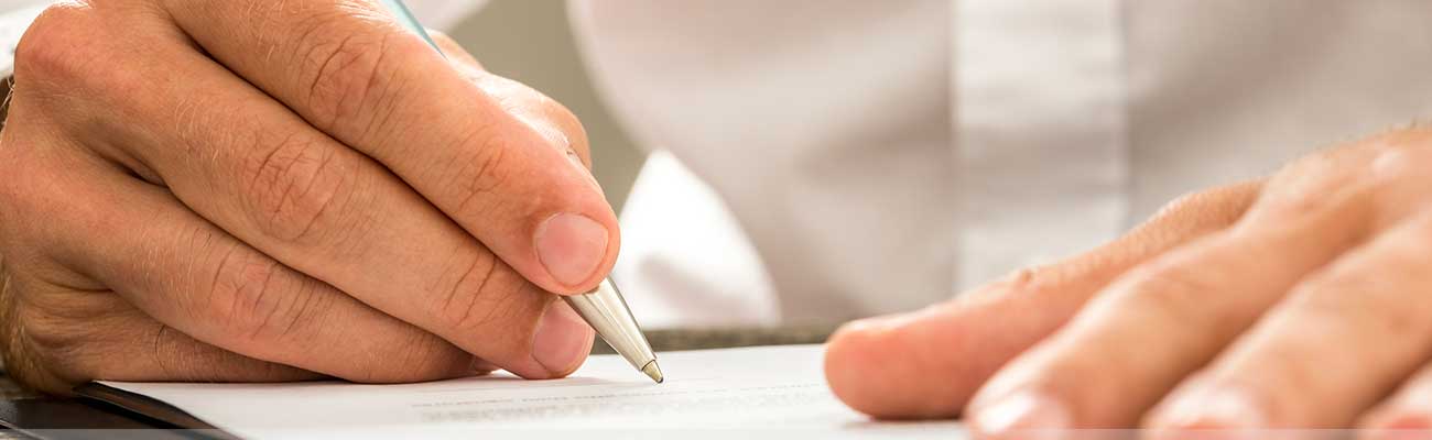 Photo of hand holding pen and signing document